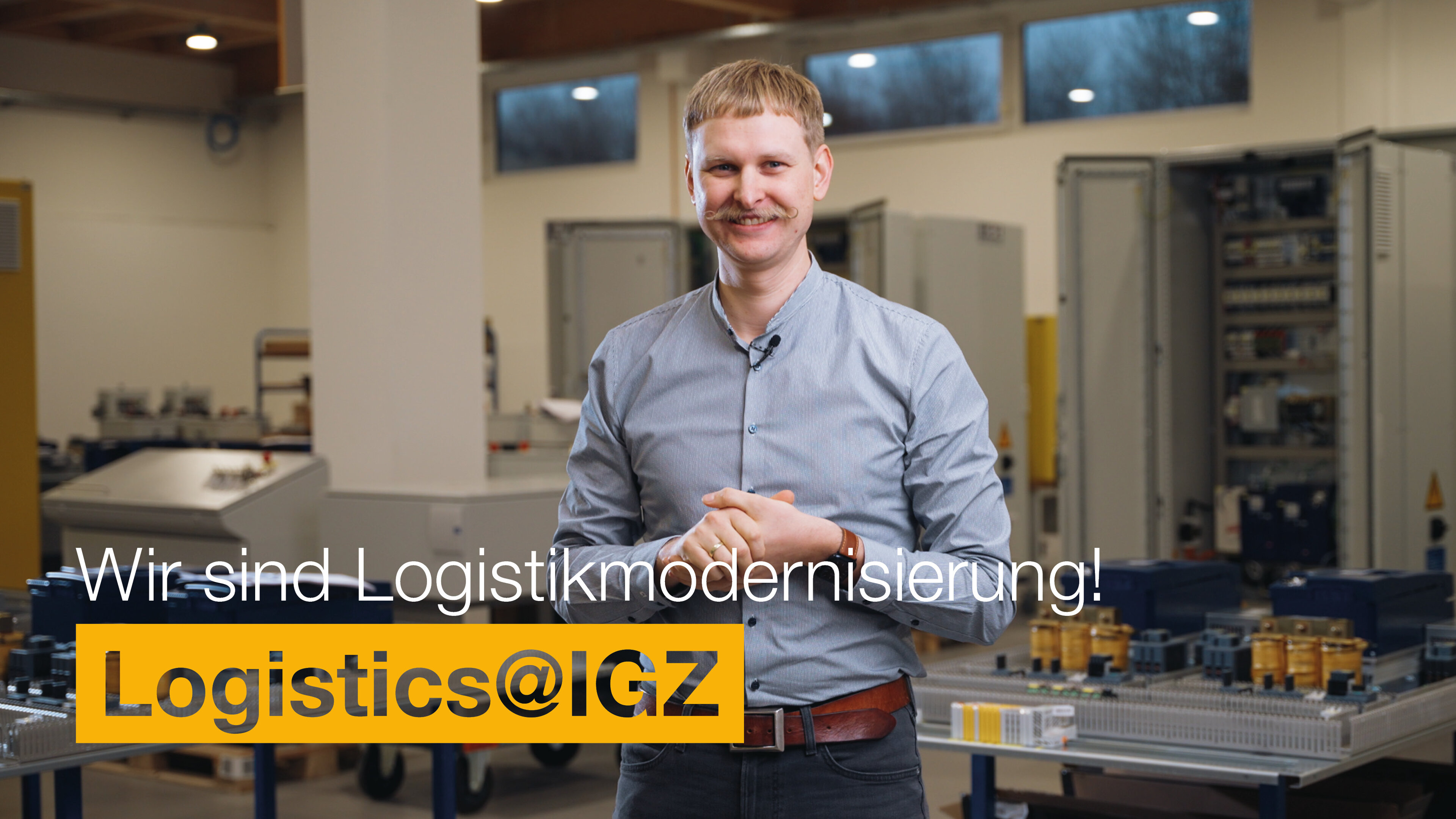 Mann mit Hemd grinst in Kamera und steht vor einer Maschine | Wir sind Logistikmodernisierung | Logistics@IGZ: | IGZ